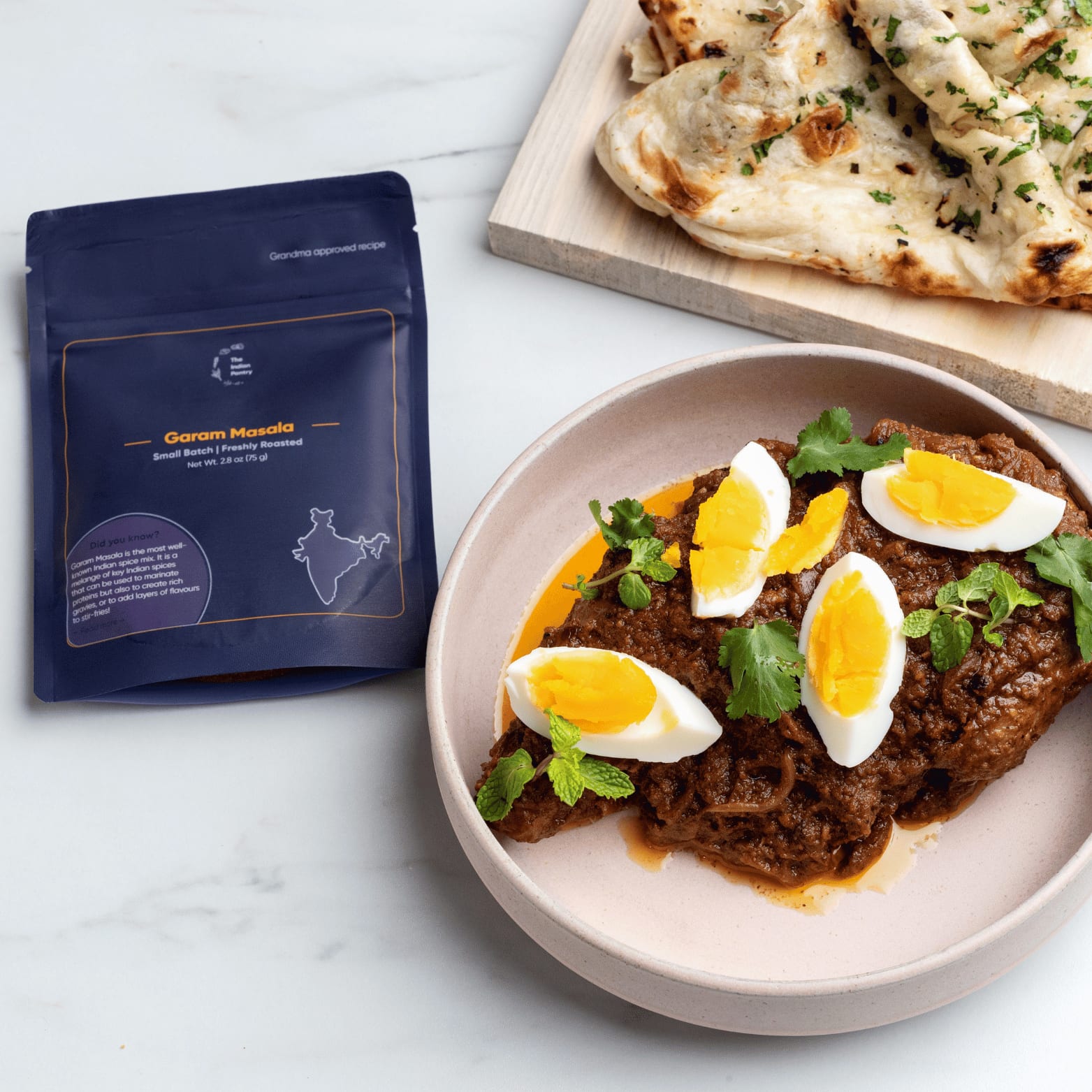 Authentic Indian beef curry served with boiled eggs, garnished with fresh herbs on a beige plate. Accompanied by naan bread and Indian spices from The Indian Pantry.